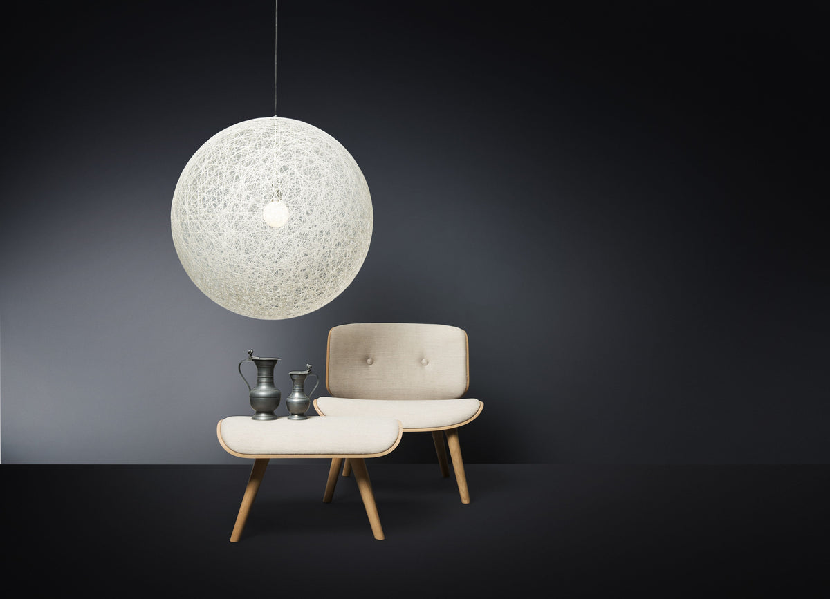 White spherical pendant light over soft beige chair and curved tabletop, set against a dark gray wall. Elegant modern design.