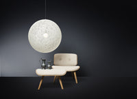 White spherical pendant light over soft beige chair and curved tabletop, set against a dark gray wall. Elegant modern design.