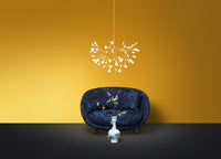 Navy blue sofa with floral patterns against a vibrant yellow wall and a sleek black floor. White chandelier overhead.