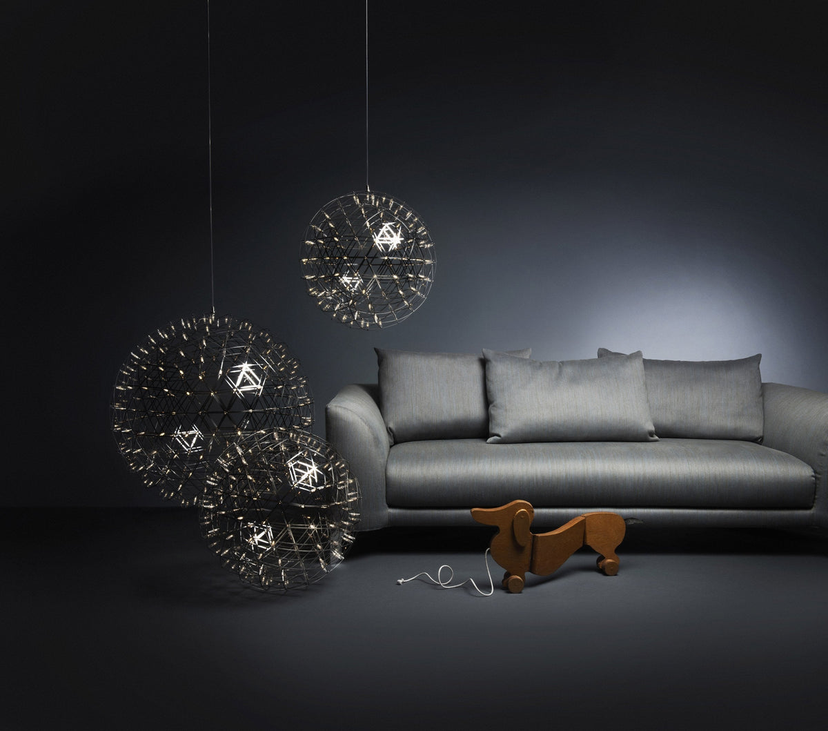 "Modern pendant lights featuring intricate black and gold designs, contrasted against a sleek gray sofa and dark backdrop."