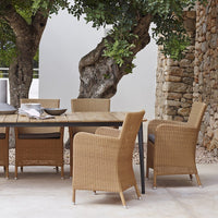 Natural woven rattan chairs with warm tan hues, paired with a rustic wood table against a stone backdrop.