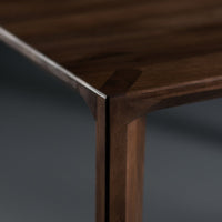 "Close-up of a dark walnut wood table edge with smooth, clean lines and rich wood grain pattern."