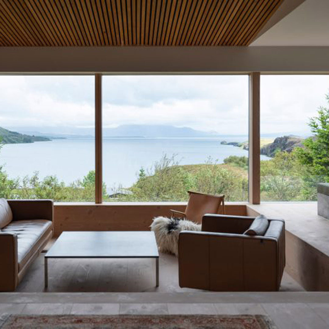 Modern living room with neutral tones, light wood accents, and stunning views of green landscape and water.