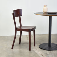 "Rich mahogany chair with a smooth finish, paired with a minimalist round table on a light gray concrete floor."