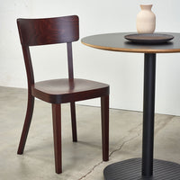 Dark mahogany chair beside a black round table with a natural wood top, set against a neutral background.