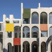 Colorful fabrics in yellow, green, and orange drape over a modern concrete structure against a clear blue sky.