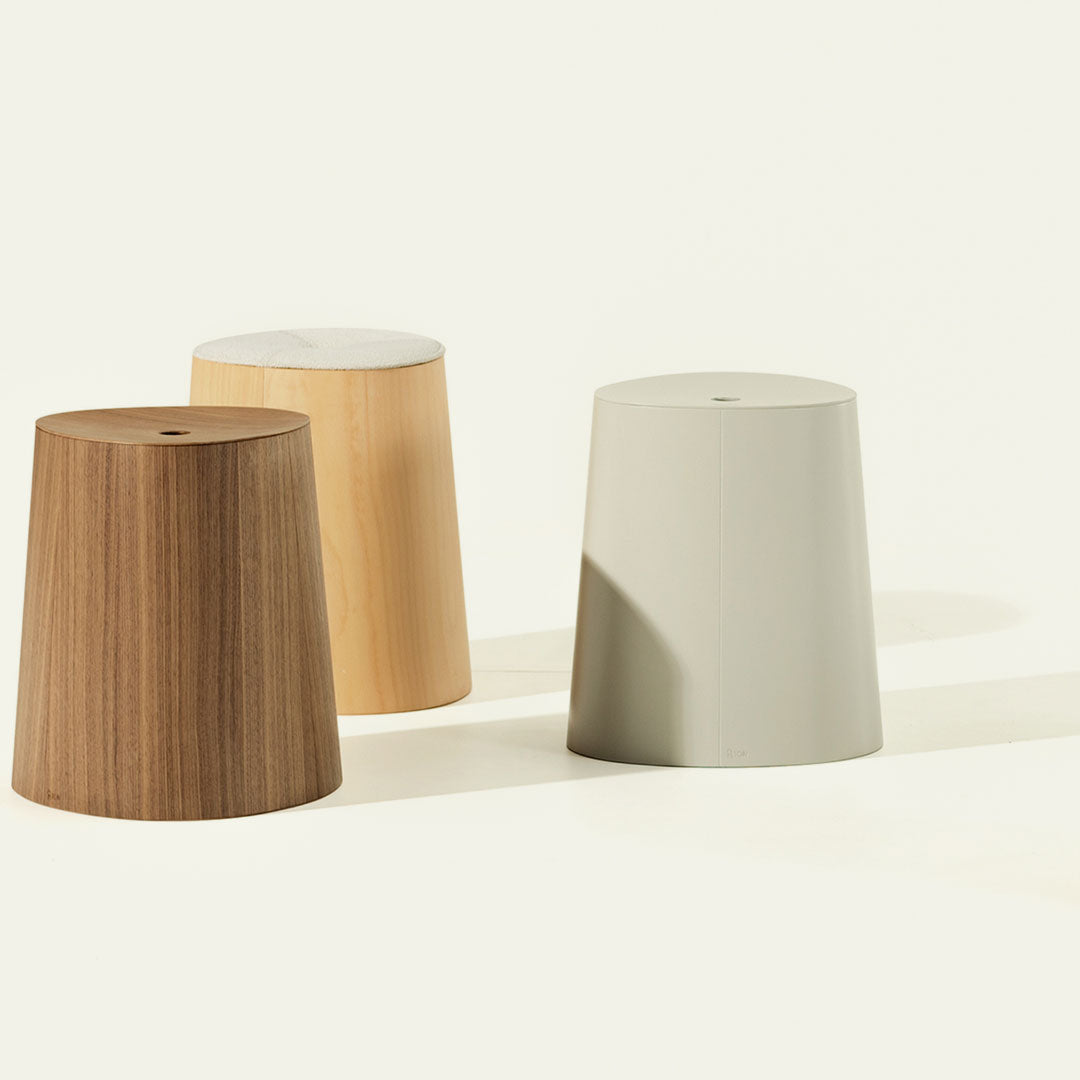 Set of three modern stools in natural wood, light wood, and soft gray, featuring smooth, minimalist designs.