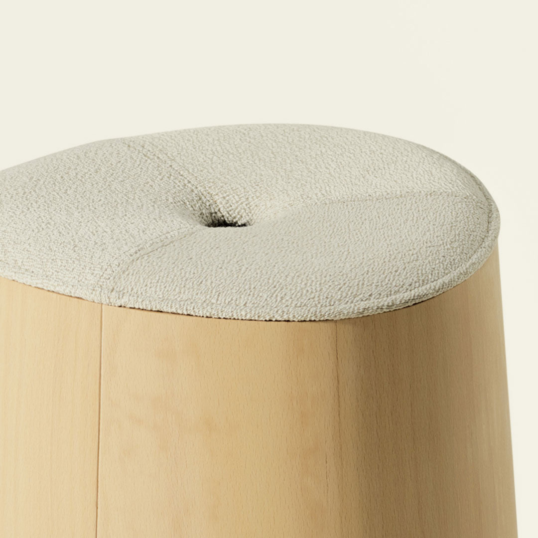 Beige textured fabric cushion atop a smooth light wood stool with a subtle rounded design.