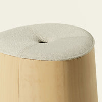 Beige textured fabric cushion atop a smooth light wood stool with a subtle rounded design.