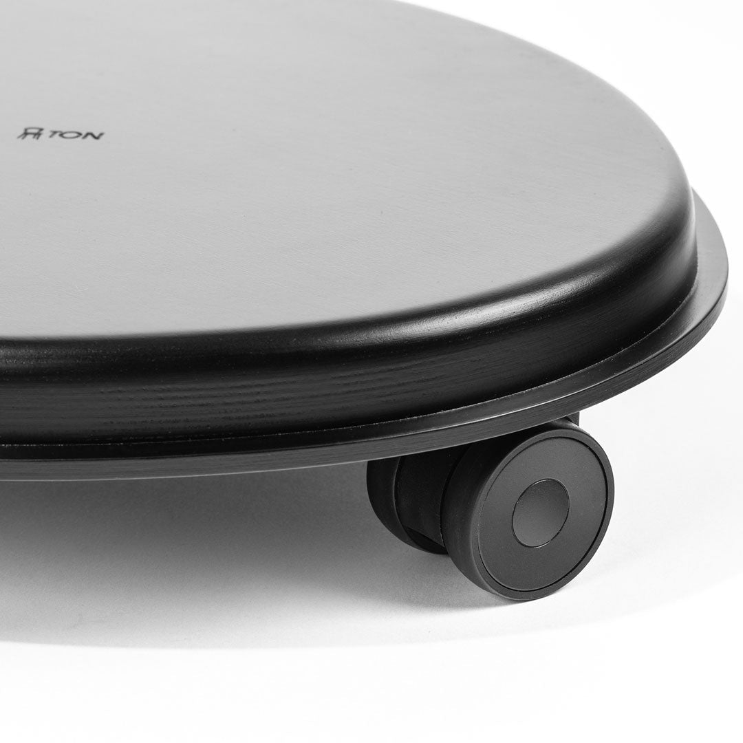 Black round platform with a smooth surface and a single wheel, featuring subtle grooved patterns along the edge.