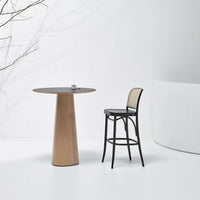 Black and natural wood dining table with smooth gray surface and a rattan-back bar stool in a minimalistic setting.