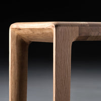 Close-up of a modern table corner featuring a mix of light oak and dark walnut wood tones with smooth, clean lines.