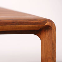Close-up of a wooden tabletop with rich brown hues and smooth, natural grain patterns. Elegant corner detail.