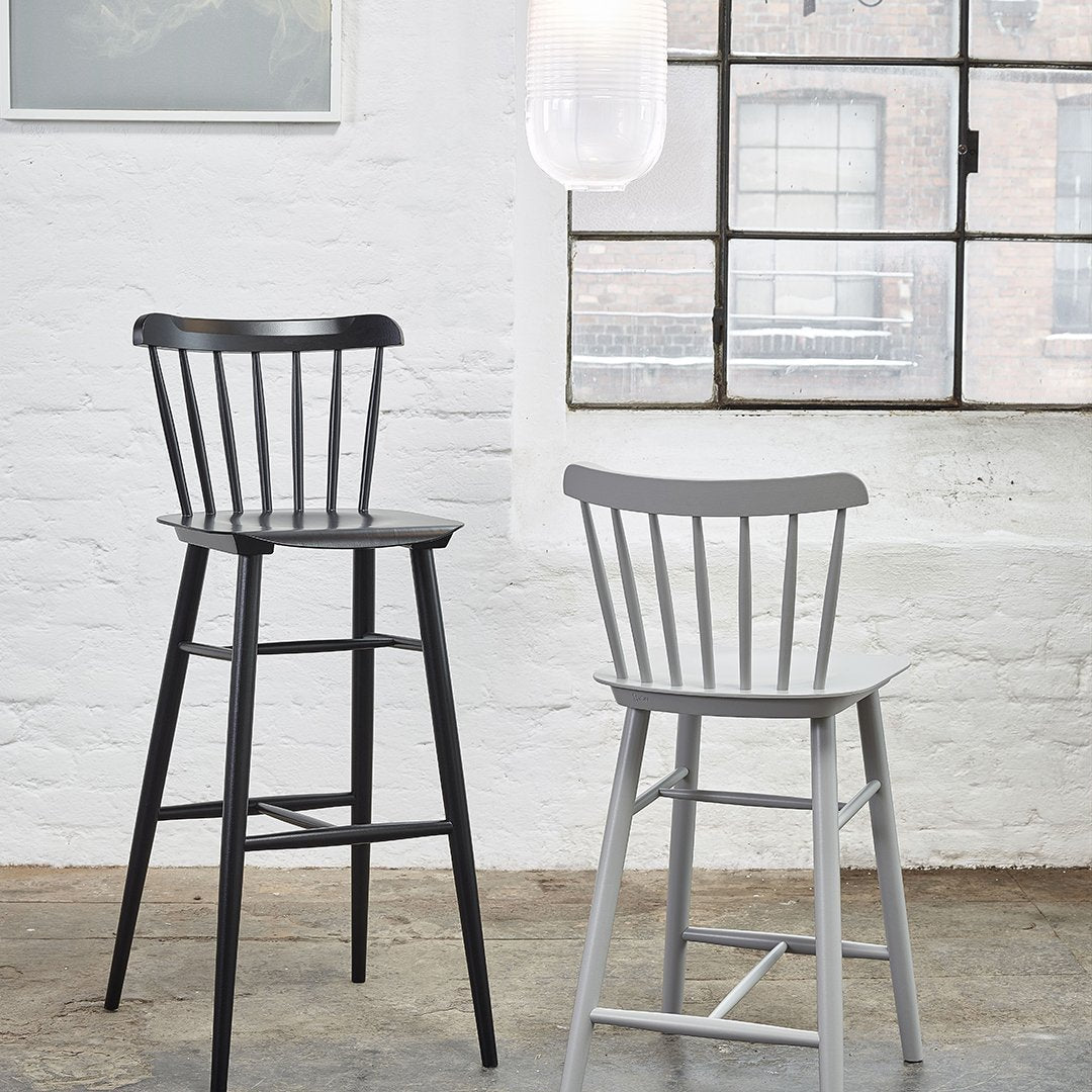 "Two modern bar stools in black and light gray with a minimalist design, set against a bright industrial backdrop."