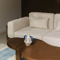White textured couch with beige and blue decorative vase on a wooden coffee table, accented by a soft blue rug.