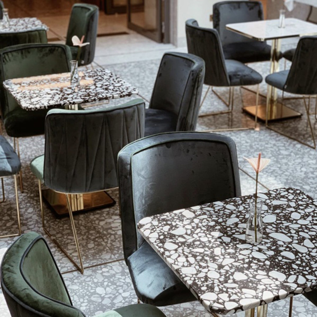 Black and white speckled tabletop with green velvet chairs, set in a stylish modern dining environment.