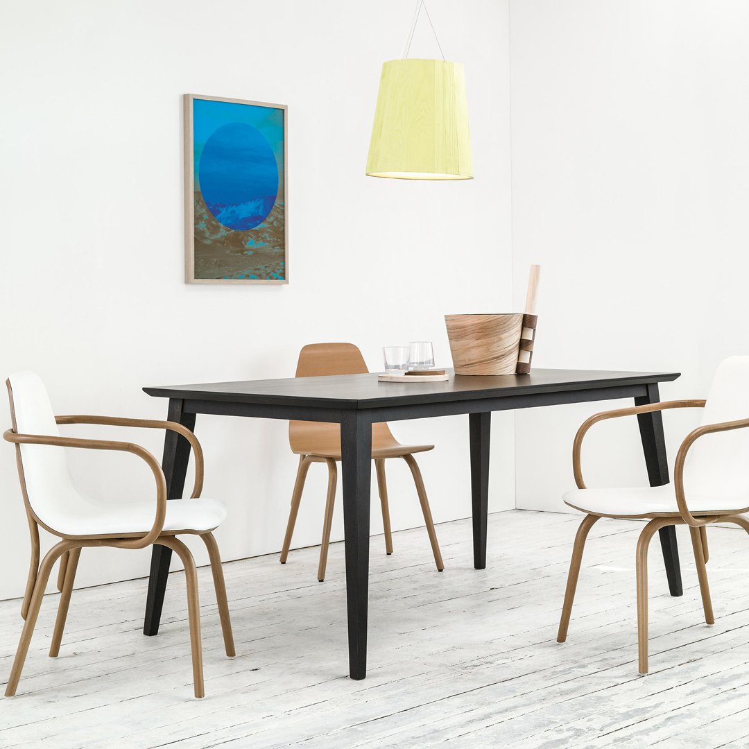 Stylish black dining table with beige and white chairs, accented by a vibrant blue wall art and a soft yellow pendant light.