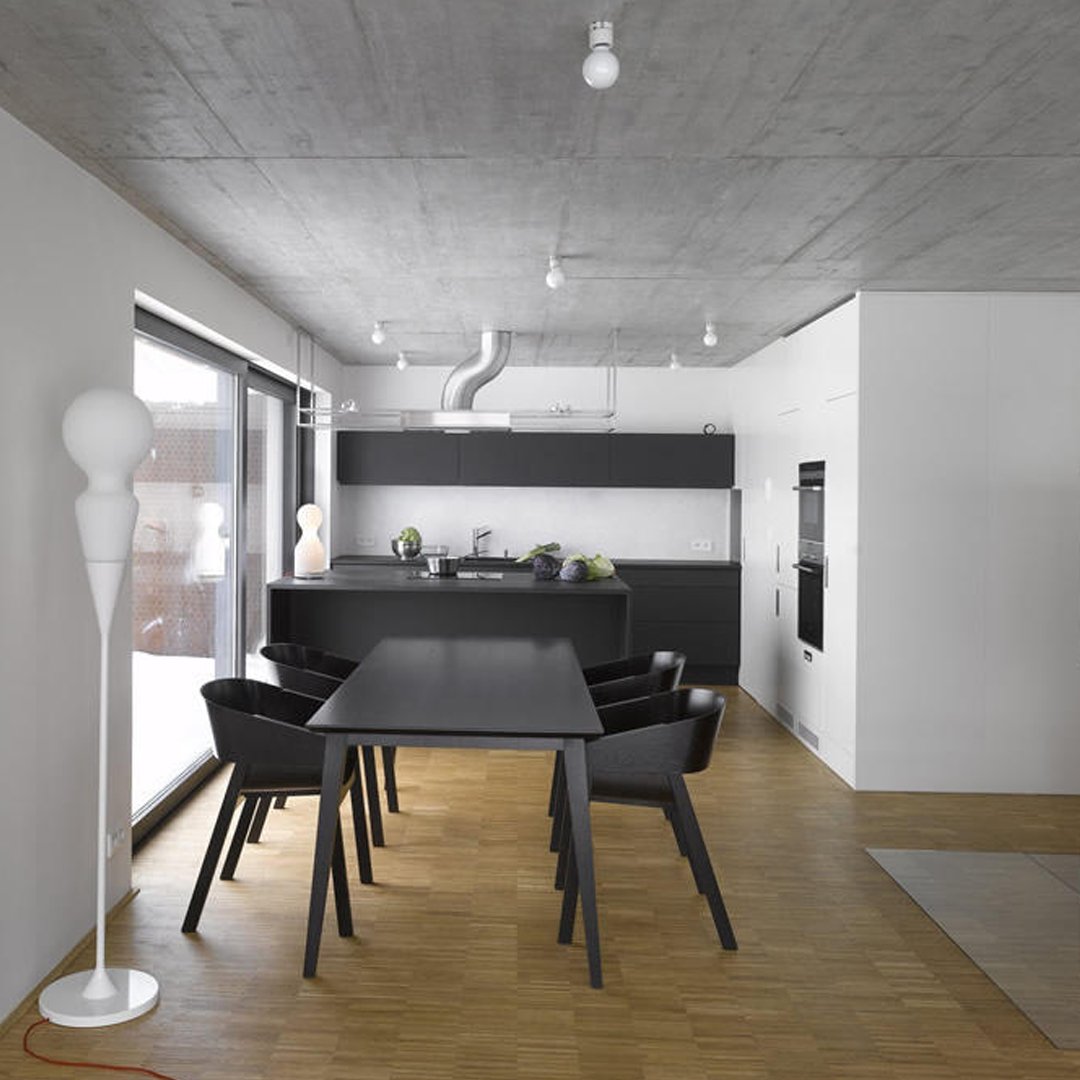 Modern black dining table with sleek black chairs, light wood flooring, and a minimalistic white backdrop.