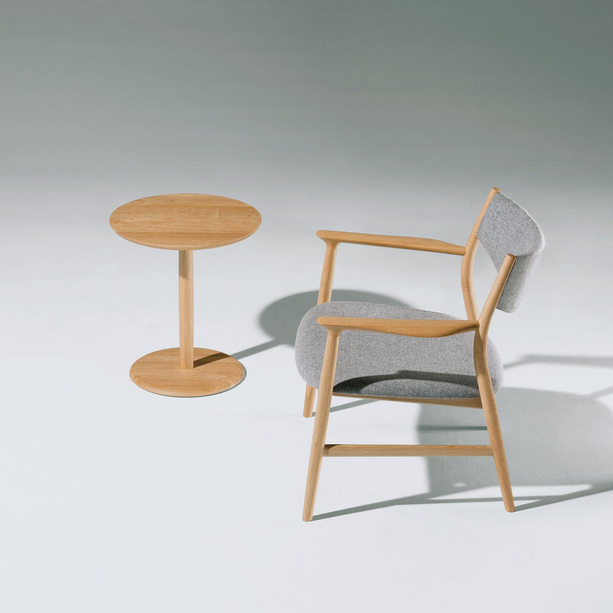 Light wood chair with gray upholstery and matching circular side table, minimalist design, smooth finishes.