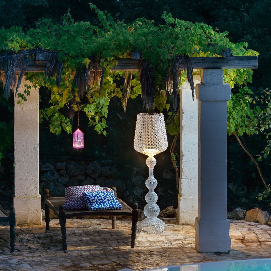 Outdoor setting with a white textured lamp, purple pendant light, and patterned blue cushions on a dark chair.