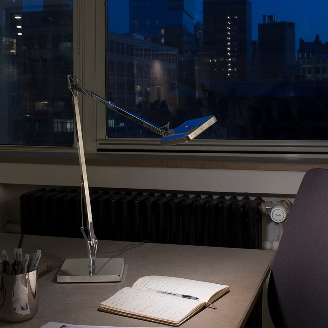 Modern desk lamp with a sleek silver finish and a blue light illuminating a minimalist workspace.