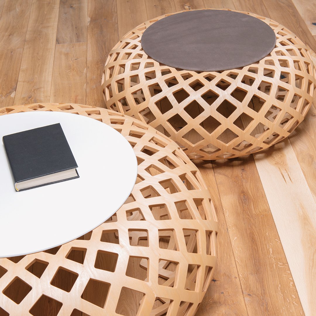 Natural wood-colored poufs with intricate lattice patterns and contrasting smooth, dark tops on a wooden floor.
