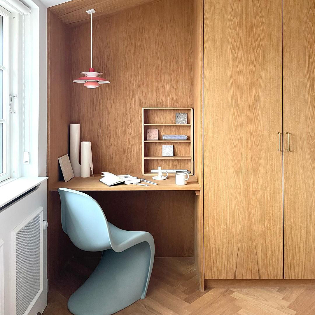 Light blue chair, pink pendant light, neutral wood tones, and muted pastel accents create a modern, minimalistic workspace.