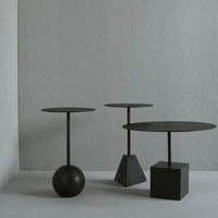 Three modern side tables in matte black, featuring round and geometric bases against a light gray background.