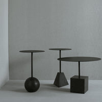 Three modern black side tables with varying shapes: a round top on a sphere, a round top on a pyramid, and a square base.