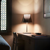 Modern gray table lamp with a sleek black and white shade, illuminating a minimalist wood desk in a warm-toned room.
