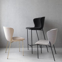 Set of three modern chairs: beige with gold legs, sleek black, and light gray upholstery against a textured gray backdrop.