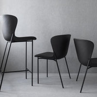 Black chairs with smooth contours and slim black metal legs against a muted gray background. Minimalist design.
