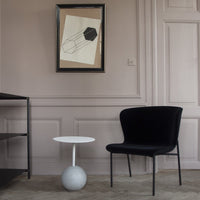 Black velvet chair with a minimalist white table and neutral-toned walls. Geometric patterns in framed art.