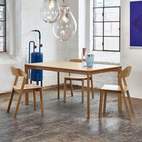 Light wooden dining table with matching chairs, featuring a minimalist design against a neutral backdrop.