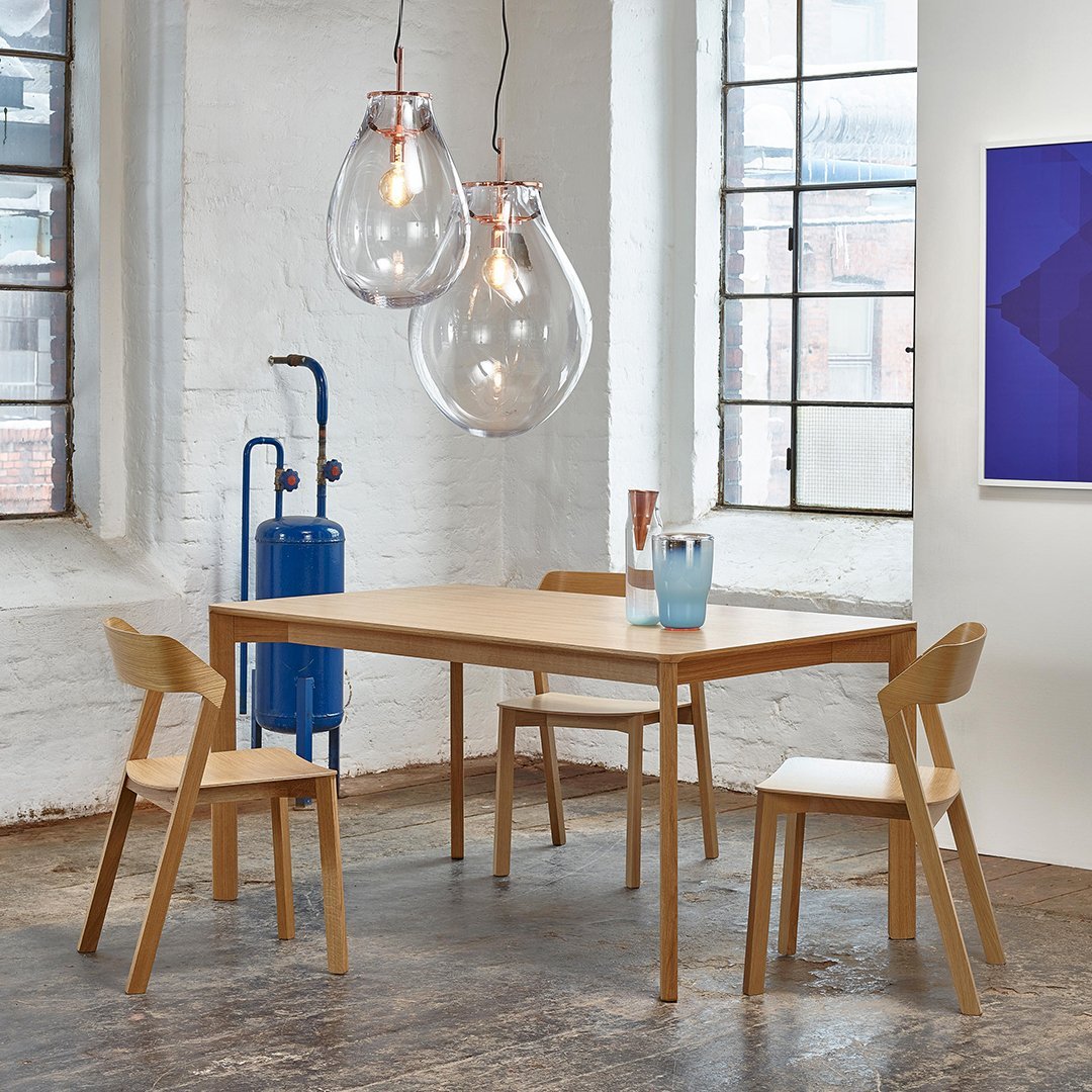 Natural wood dining table with sleek chairs, geometric patterns, and clear glass light fixtures in a modern setting.