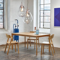 Natural wood dining table with sleek chairs, geometric patterns, and clear glass light fixtures in a modern setting.