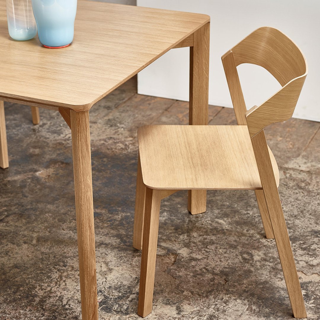 Light wood dining table and chair with a minimalist design, featuring smooth surfaces and natural wood grain patterns.