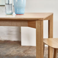 Natural oak wood dining table with clean lines, complemented by soft pastel blue and vibrant red accents in decor.