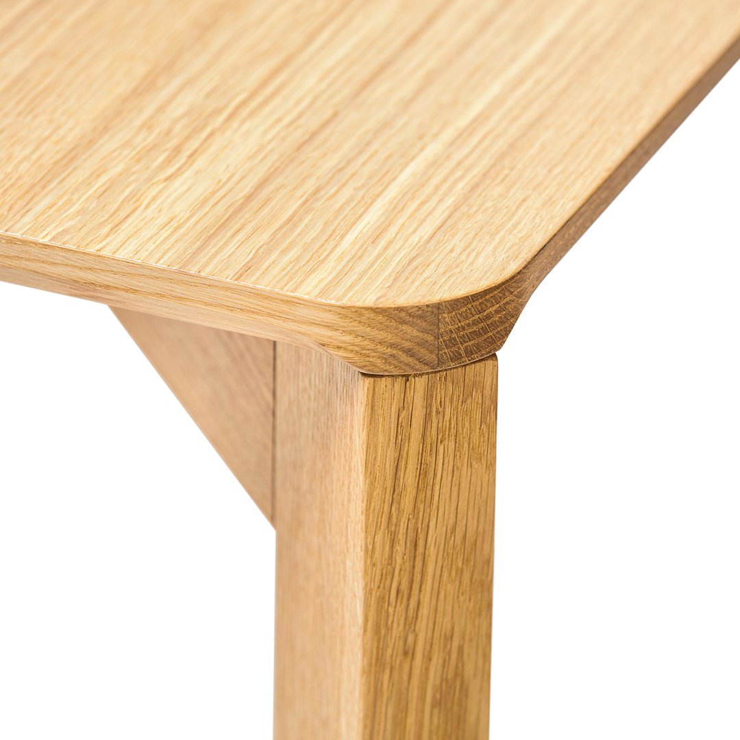 Light oak wood table corner with a smooth, natural grain pattern, showcasing warm, earthy tones.