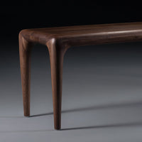 Elegant walnut wood table with smooth, curved edges and a rich, dark brown finish, contrasting against a grey backdrop.