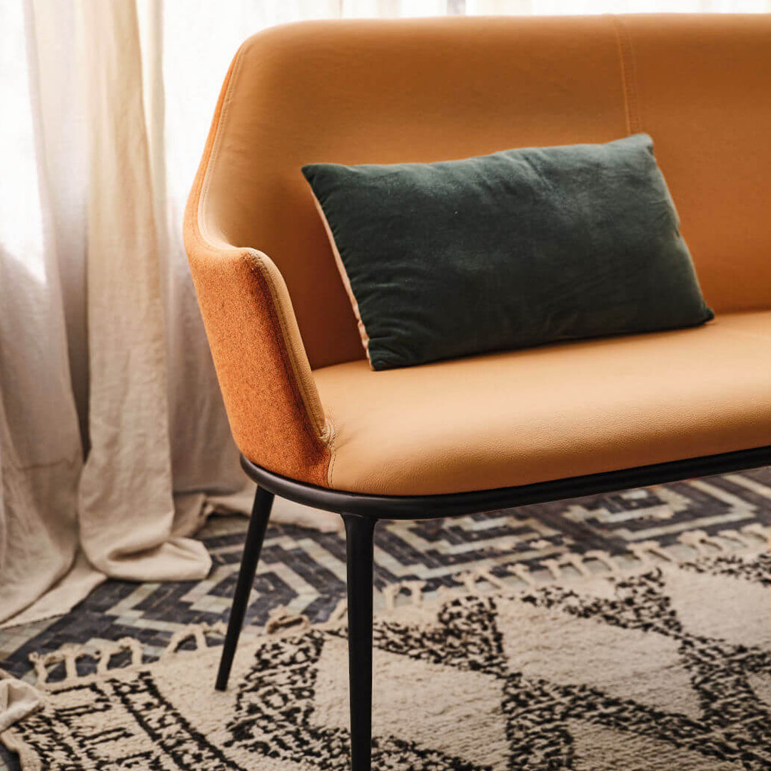 Orange and tan upholstered sofa with a green cushion, set against a patterned area rug.