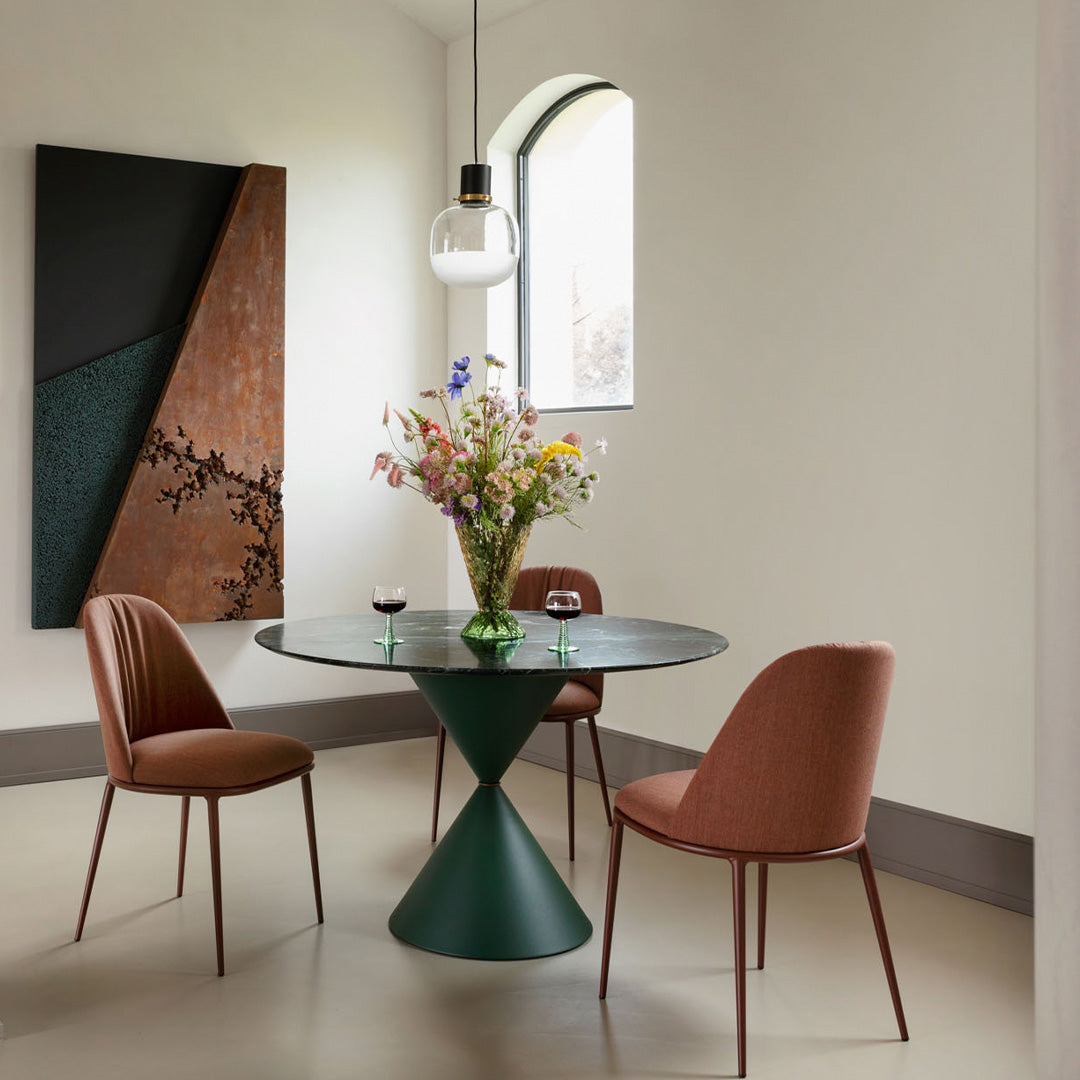 Modern round table in green with brown chairs; floral centerpiece adds color to neutral tones and geometric patterns.