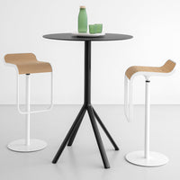 Black round table with three tripod legs, paired with two beige and white bar stools. Smooth, modern minimalist design.