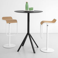 Black round table with three-legged design, paired with white and natural wood bar stools against a minimalist backdrop.