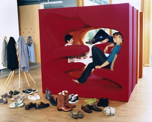 "Vibrant red seating area with abstract cutouts, contrasted by a variety of shoes in earthy tones on the floor."