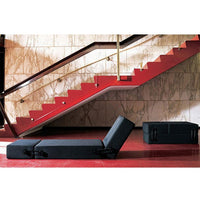 Black foldable lounge chair against bold red and marble patterned backdrop, featuring stylish modern design.