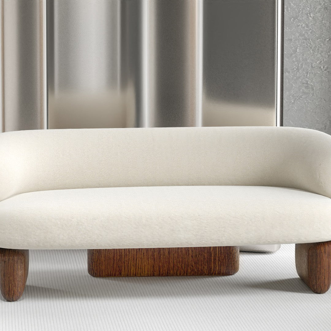Cream-colored sofa with a smooth, rounded design and rich wooden legs, set against a sleek metallic backdrop.