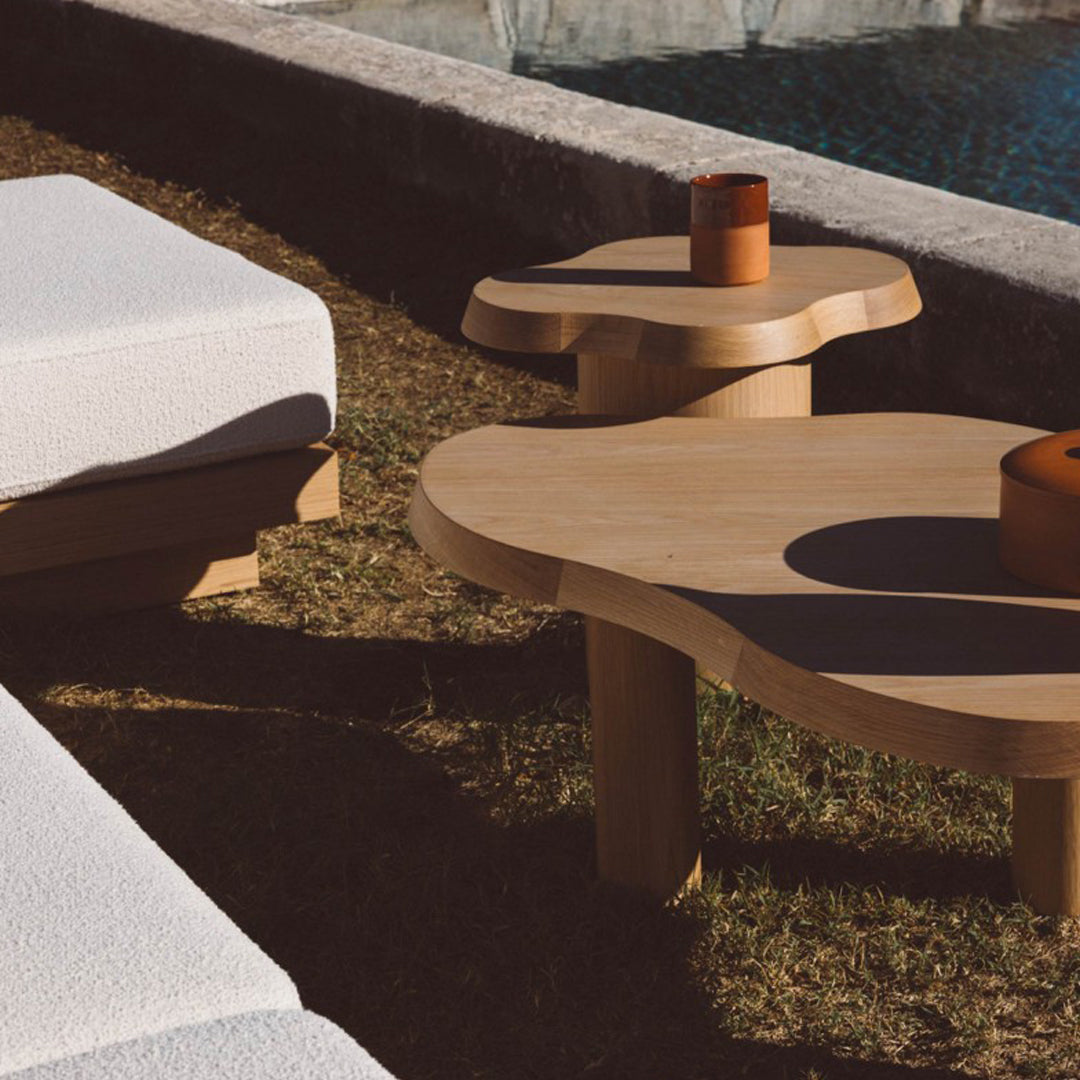 Light wood coffee tables with organic shapes, set against green grass, featuring simple, elegant design.