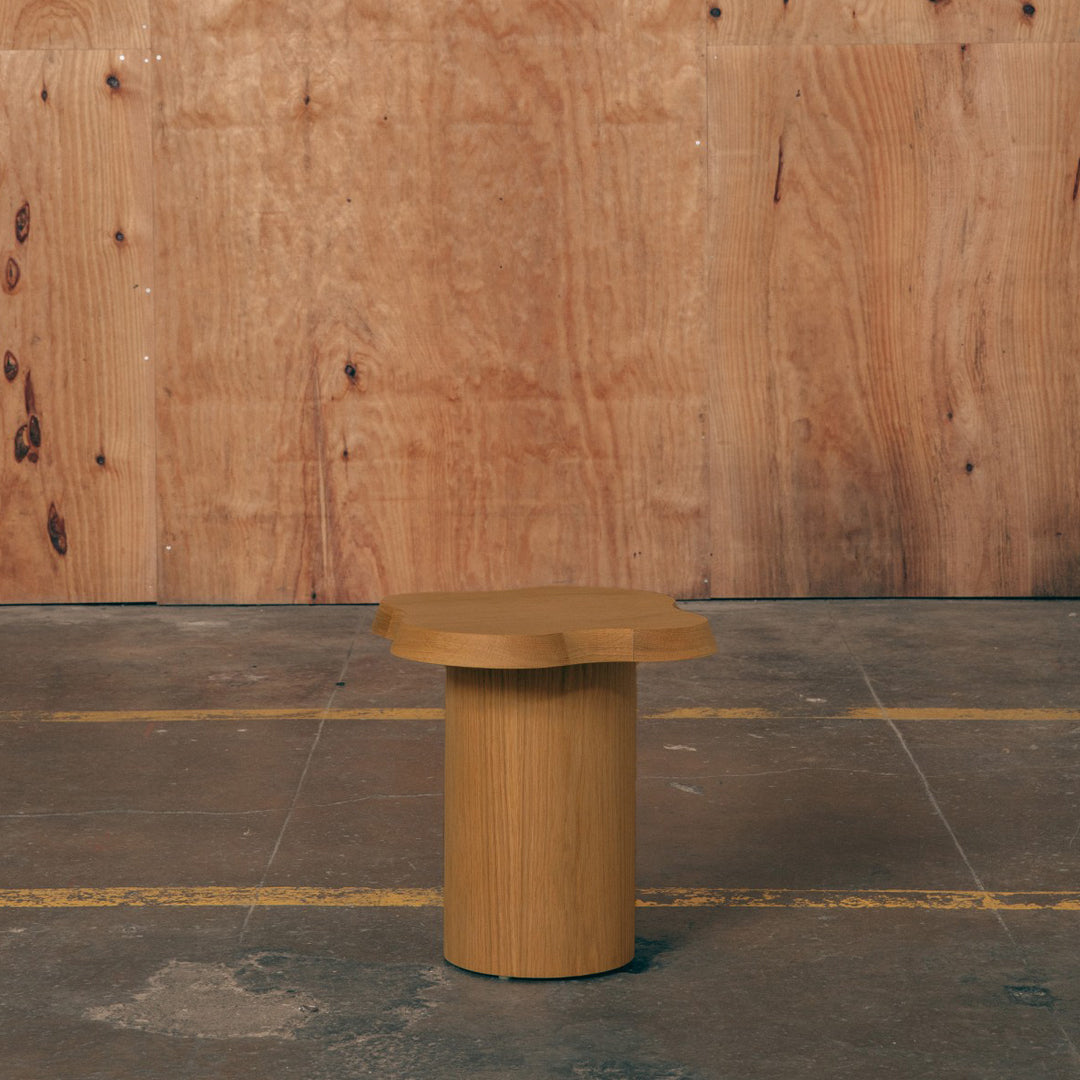 Natural wood round side table with a smooth finish and simple, modern design against a rustic wood backdrop.