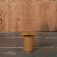 Natural wood round side table with a smooth finish and simple, modern design against a rustic wood backdrop.